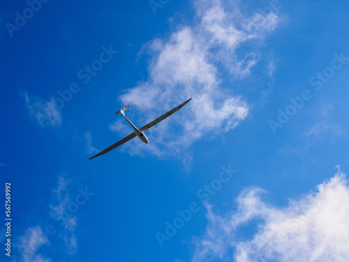 A white flying glider seen from below with blue sky and white clouds.