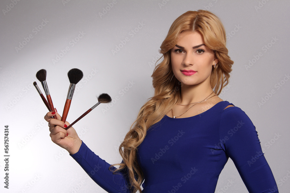 portrait of a blonde makeup artist girl with blonde hair in a blue dress with face brushes in the studio room, with makeup and hairstyle, red lips and manicure, draws portrait of a blonde makeup artist girl with blonde hair in a blue dress with face brushes in the studio room, with makeup and hairstyle, red lips and manicure, draws