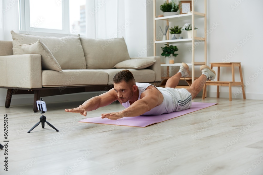 Man sports, watching a workout tape on his phone and repeating exercises blogger, pumped up man fitness trainer works out at home, the concept of health and body beauty