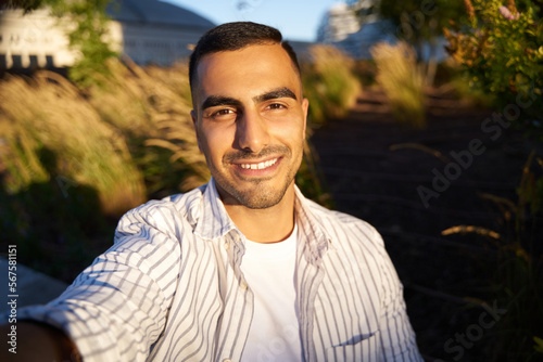 Smiling handsome middle eastern man influencer recording video, communication online on the street . Modern technology concept  