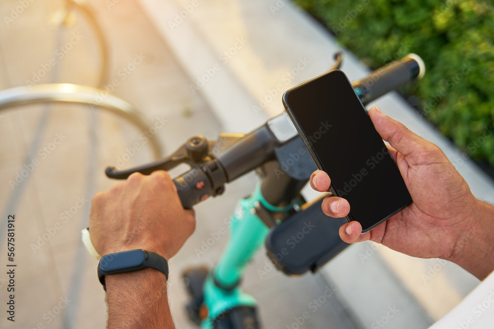 Cropped view of the man hand holding mobile phone unlocking electric scooter while preparing to the ride outdoors. Transportation concept
