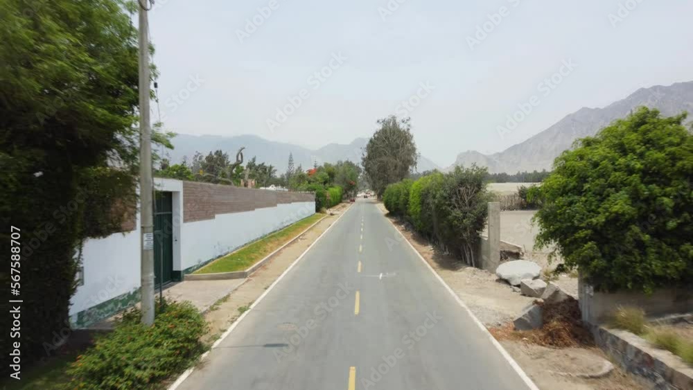 A motorcycle driver riding down a street as a drone follows flying backwards. In the horizon mountains can be seen in the distance. Located in Cineguilla in Lima Peru. A motorcycle driver riding down a street as a drone follows flying backwards. In the horizon mountains can be seen in the distance. Located in Cineguilla in Lima Peru.