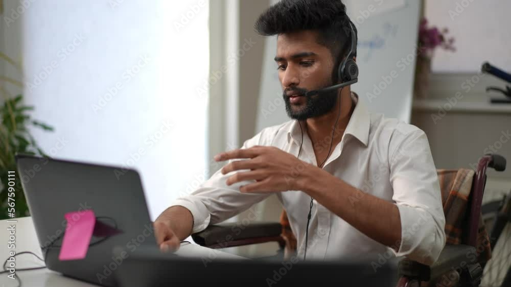 Tech support professional in headphones talking typing on laptop keyboard sitting in home office indoors. Portrait of young handsome Middle Eastern man in wheelchair working remotely Tech support professional in headphones talking typing on laptop keyboard sitting in home office indoors. Portrait of young handsome Middle Eastern man in wheelchair working remotely