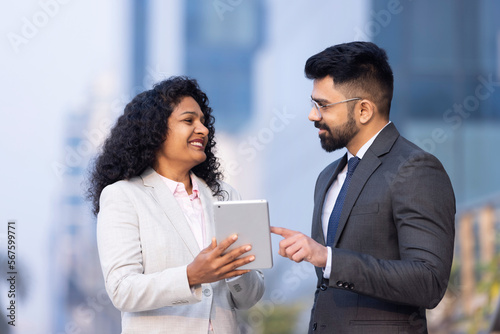 Indian businessman and businesswoman using digital tablet on city street.