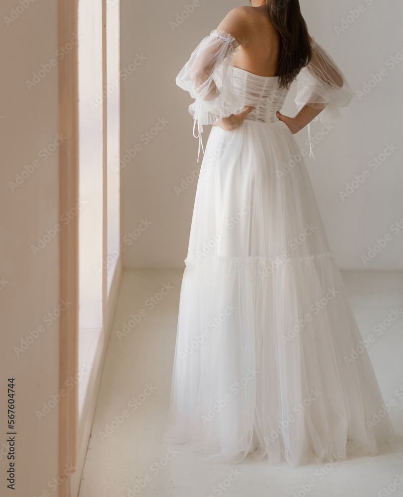Back view of beautiful brunet bride dressed in the white long wedding dress with the naked back. Light chiffon wedding dress with with wide collapsible sleeves. Back view of beautiful brunet bride dressed in the white long wedding dress with the naked back. Light chiffon wedding dress with with wide collapsible sleeves.