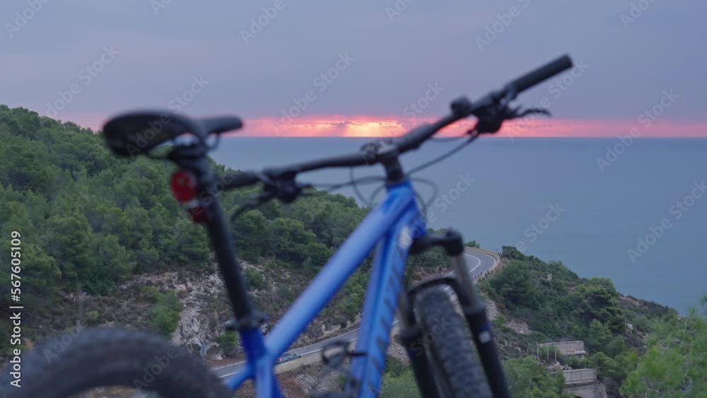 Time lapse of mountain bike parked in wild as cars drive down below and red morning sun rises over the horizon Time lapse of mountain bike parked in wild as cars drive down below and red morning sun rises over the horizon