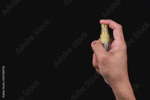 One hand holding a bottle of hand sanitizer and ready to spray with isolated black background