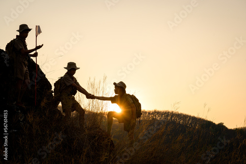 Asian Scout schoolgirl hiking with backpack Three students showed help to each other. Holding hands to help pull each other up from the cliff photo