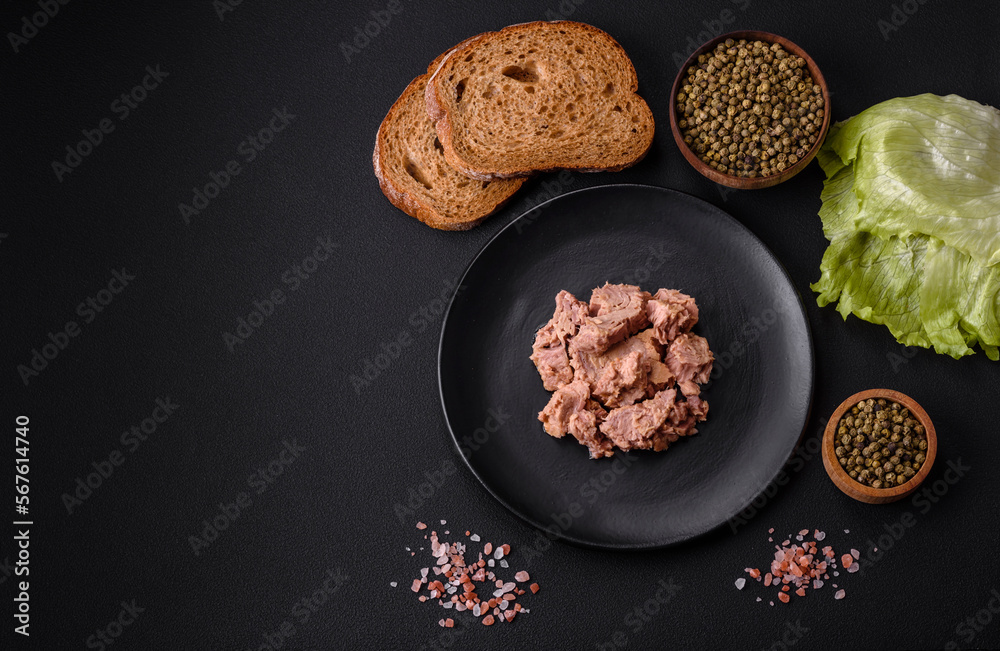 Delicious canned tuna meat on a black ceramic plate on a dark concrete background