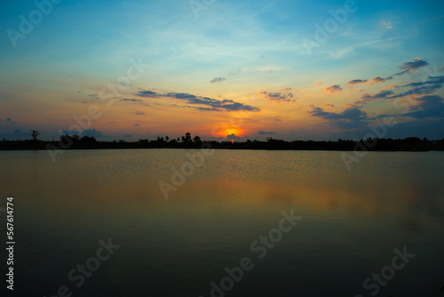 beautiful teal and orange color sunset at the lake on agricultural land in the village © Kreative