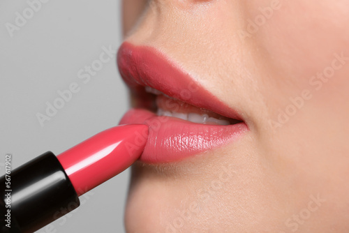 Young woman applying beautiful glossy lipstick on light background, closeup