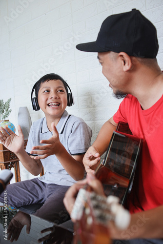 Dad and son singing and playing guitar together while doing video online streaming. Asian family spending quality time at home while recording video on digital camera.