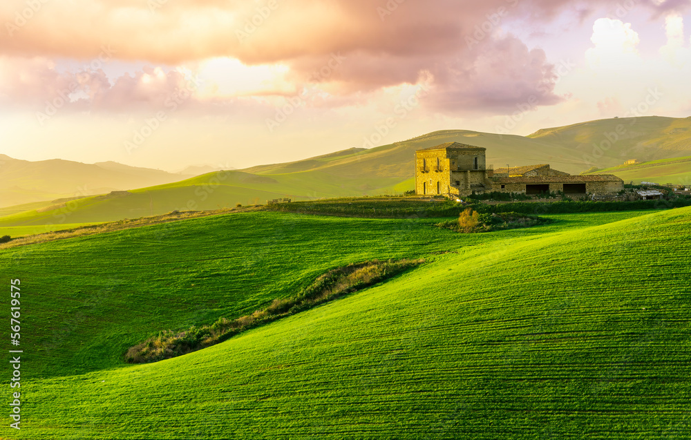 Fototapeta premium sceniv view at a nice farm in green fields in hills and highlands, landscape of spring green hills with mountain bright sunset on backdrop