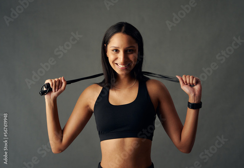 Portrait of happy young biracial woman in sports bra holding jump rope behind head in studio