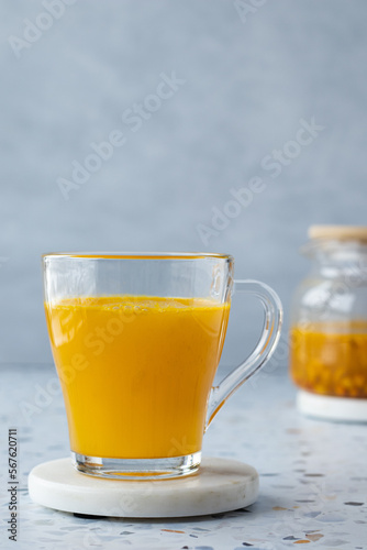 Hot sea ​​buckthorn tea with ginger and honey in a glass cup. Teapot on a terrazzo table. Grey background. Close up. Vitamin drink, immune support, cold remedy. Health supplements. Copy space