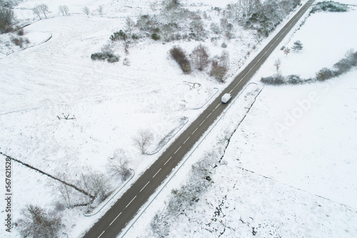 aerial drone view of a vehicle driving on a highway in a snowy landscape © VicVaz
