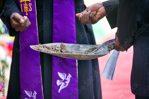 priest and mourner holding a spade with ground to bless the grave photo