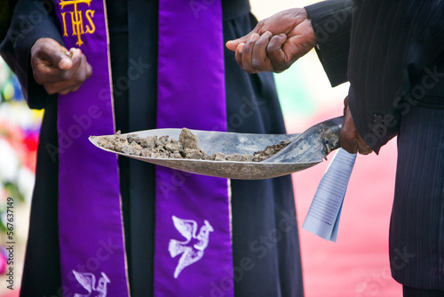 priest and mourner holding a spade with ground to bless the grave