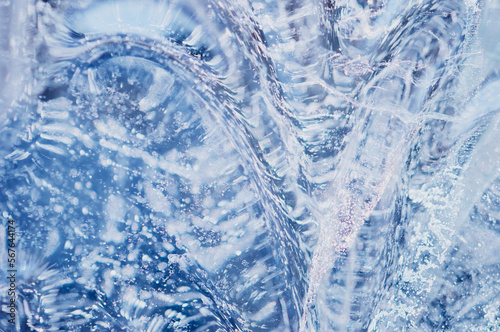 Bubbles and cracks inside natural ice. Geometric wavy pattern of glare and light distortion. Abstract background. Close up. Selective focus.