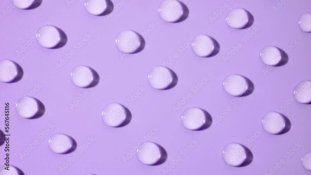 Macro crane shot of moving transparent drops on violet background | Abstract skincare gel ingredients formulating concept Macro crane shot of moving transparent drops on violet background | Abstract skincare gel ingredients formulating concept