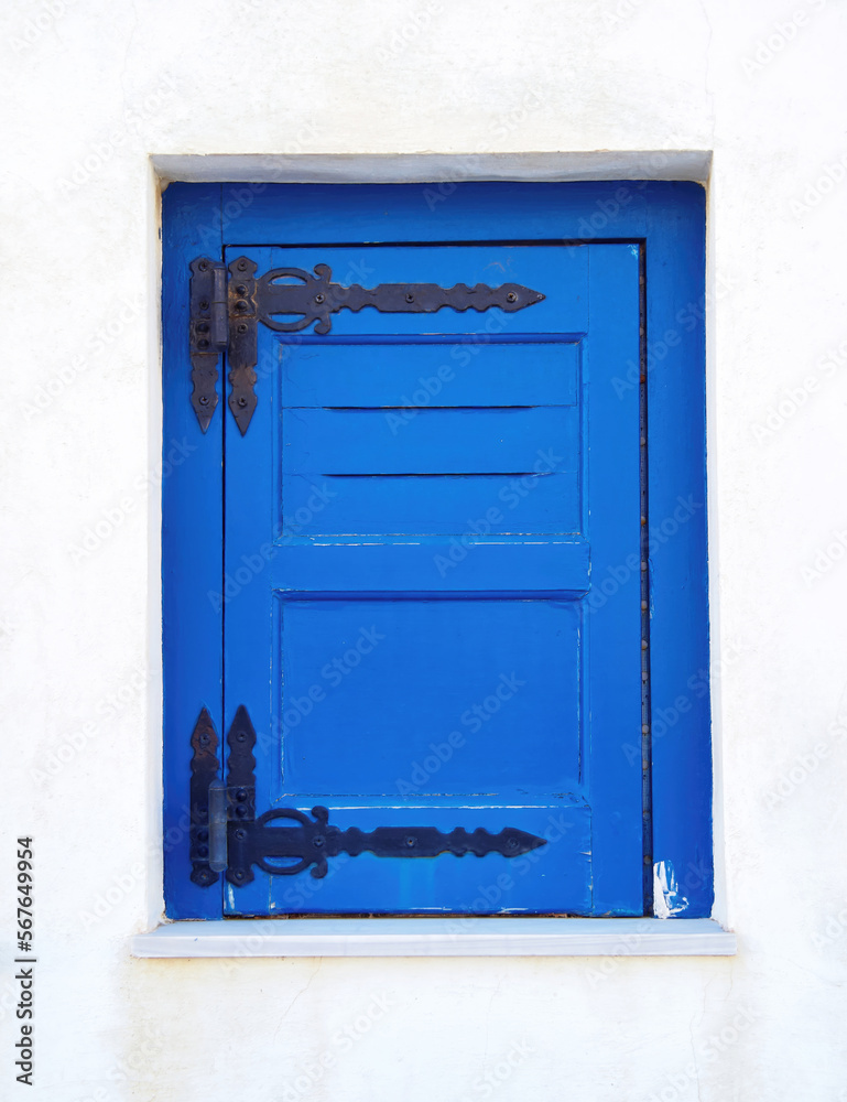 Bright blue painted window shutters on a white washed wall. Travel in Greek islands.