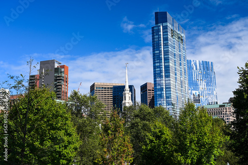 Boston, MA / US 09 07 2022: Skyline of Boston with skyscrapers and office buidlings behind green trees of the Boston Public Garden.