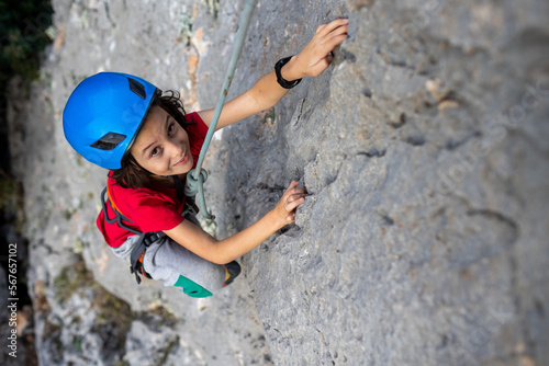 child rock climber in a blue protective helmet overcomes the route in the mountains. children's sports in nature.
