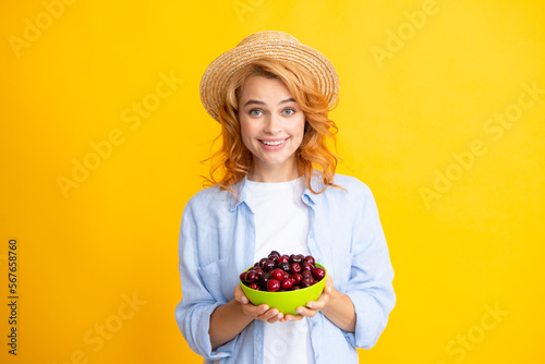 Charming woman with cherry plate isolated on yellow.