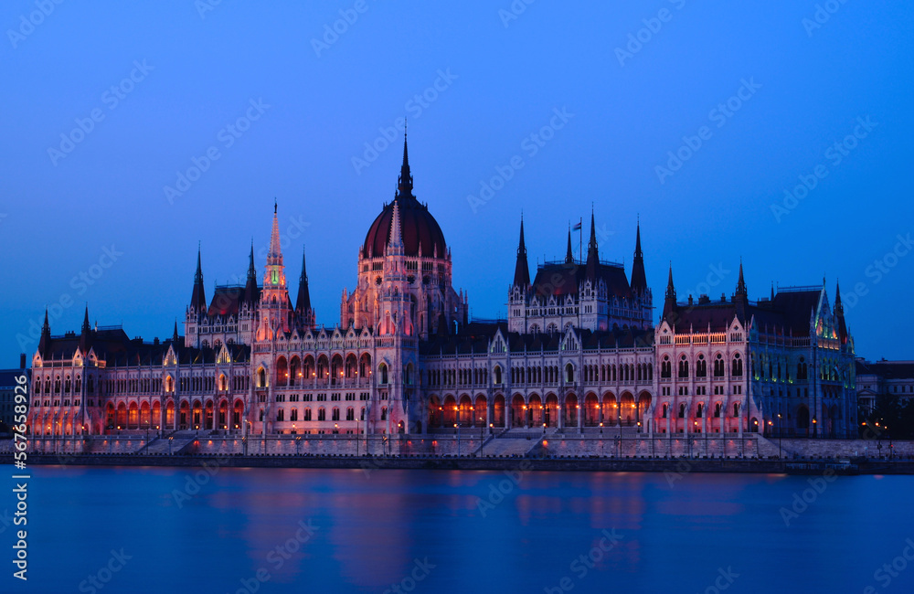 Fototapeta premium The Hungarian Parliament in Neo-Gothic style from across the Danube at blue hour. long exposure. blue sky. travel destination. Famous and popular Budapest landmark and tourist attraction. City skyline