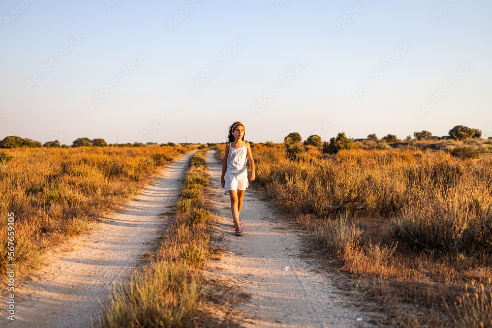 Lonely girl walking on a country road at sunset.