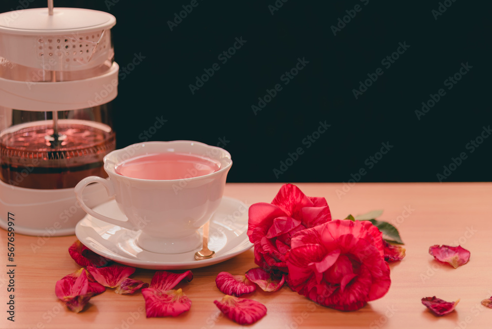 A white teacup of pink rose tea on saucer on a wooden table with two-tone red roses and falling petals,Hot drink good healthy and feel relaxed has herbal medicinal properties that are nice for health. - obrazy, fototapety, plakaty 