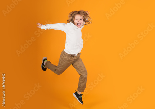 Full length of excited kid jumping. Little child jumping over a yellow background.
