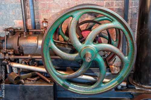 Small steam engine. Green metal flywheel. Industrial exhibition. Red brick wall in the background. photo