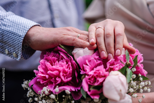 Hands of newlyweds with wedding rings on a pink wedding bouquet of peonies © Galka3250