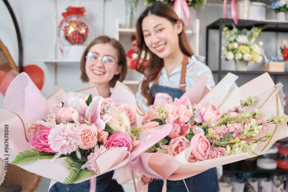 Two young beautiful women florist partners giving floral bunch with a smile, selective focus on a blossom bouquet, lovely business entrepreneur, flower shop happy work, brightly colorful flora store. Two young beautiful women florist partners giving floral bunch with a smile, selective focus on a blossom bouquet, lovely business entrepreneur, flower shop happy work, brightly colorful flora store.