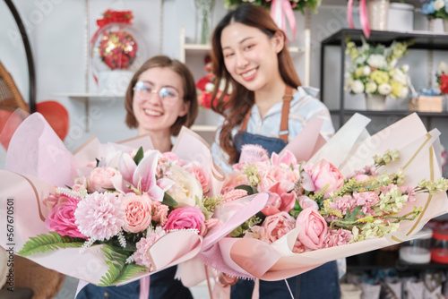 Two young beautiful women florist partners giving floral bunch with a smile, selective focus on a blossom bouquet, lovely business entrepreneur, flower shop happy work, brightly colorful flora store.