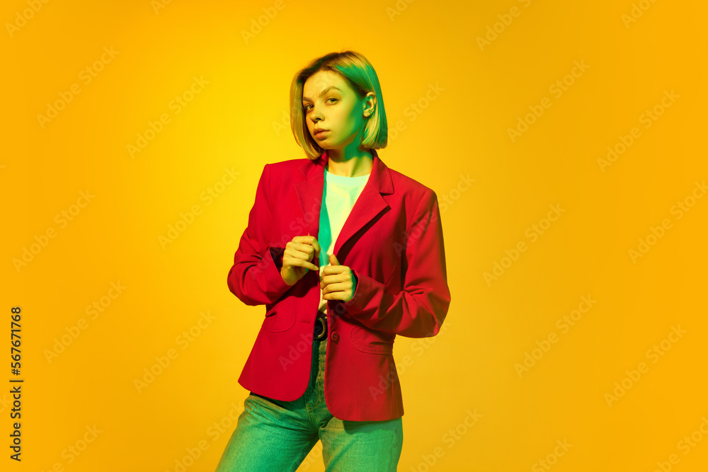 Young charming girl with blonde hair wearing red jacket posing over yellow background. Concept of youth, student college life, business and education