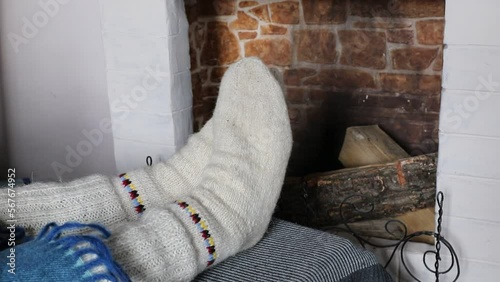 Warm knitted socks are worn on the feet. A man warms his feet near the fireplace.