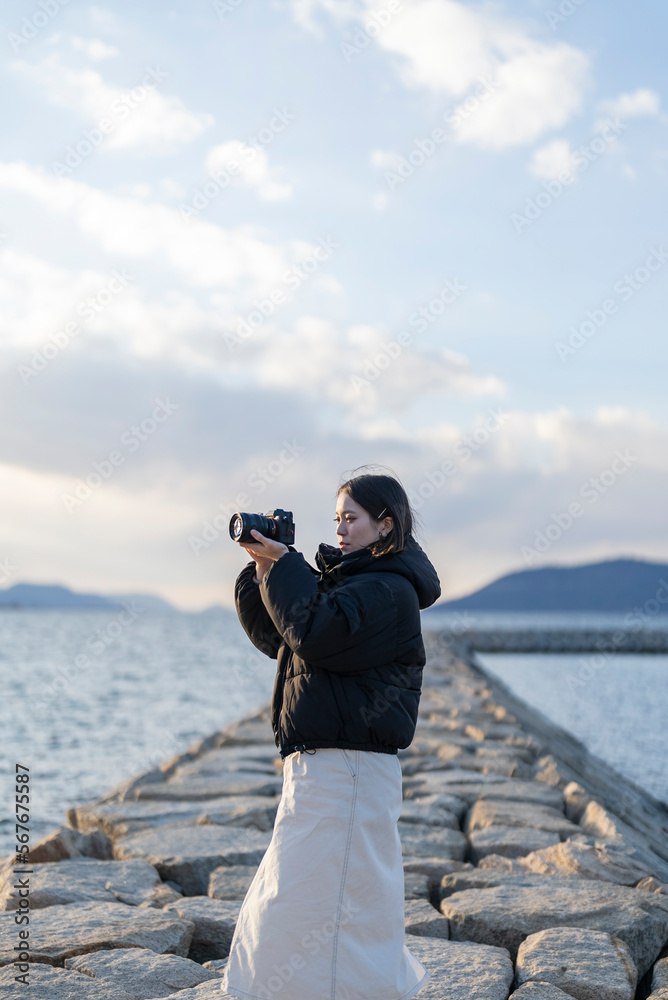 夕暮れの海で写真を撮る女性