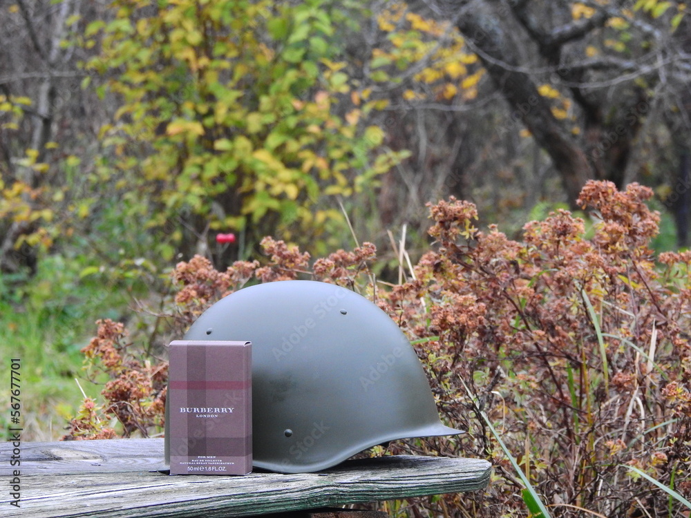 Fototapeta premium Bottle of Burberry London eau de toilette with a 1960s steel helmet and other Russian militaria, Taldom, Russia - October 31, 2020