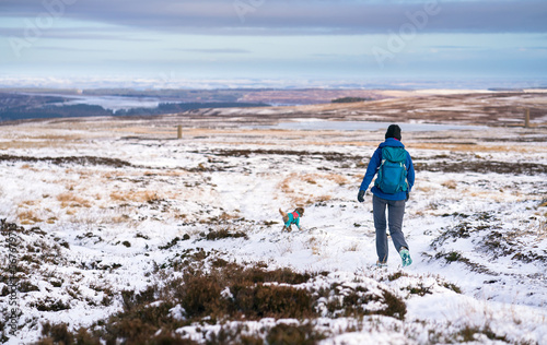 A hiker and their dog coming down from the summit of Bolt's Law near Blanchland in winter, Northumberland in England UK.