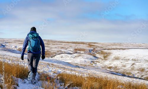 A hiker walking across the moors below the summit of Bolt's Law towards Boltshope in winter near Blanchland, Northumberland in England UK.