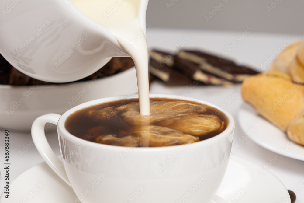 Cream from the milk jug is poured into coffee, making coffee with cream, cappuccino. Cream from the milk jug is poured into coffee, making coffee with cream, cappuccino.