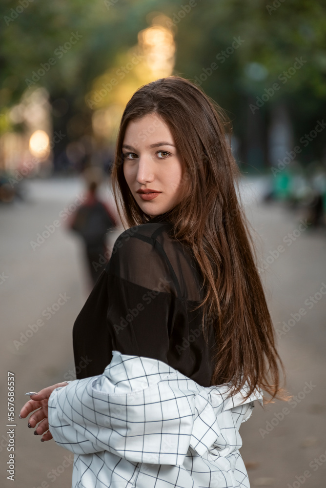 Portrait of an attractive young woman with long hair on park background. Gaze of raven-haired.