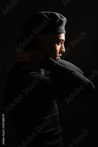 side view of african american man in pullover and beret posing with hands behind neck isolated on black