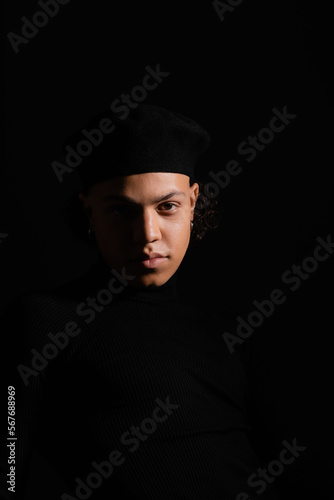 portrait of young african american man with shaded face wearing stylish beret isolated on black
