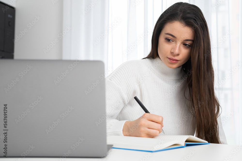 Serious young lady in stylish wear attends online lecture and makes notes with copy space. Serious young lady in stylish wear attends online lecture and makes notes with copy space.