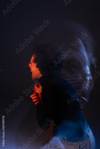 double exposure of wounded and angry african american man shouting on black background with red and blue light