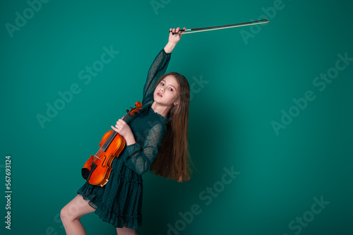 A girl in a green dress plays the violin on a plain green background.