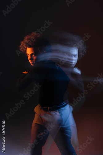 long exposure of young and injured african american man with bipolar disorder looking at camera on black with orange and blue light